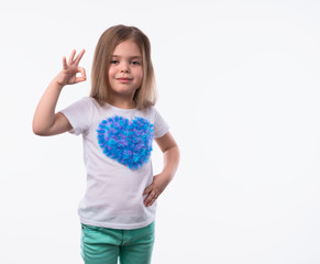 Close up shot of little positive girl with long fair hair looking at camera artistically and shows ok-gesture. The portrait is made on a white background.