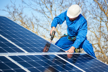 Male engineer in blue suit and protective helmet installing photovoltaic panel system using...