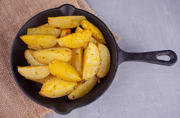 Homemade baked potato wedges with herbs on black iron pan on the gray background. Top view.