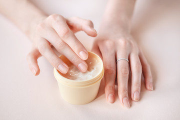 Beautiful groomed woman's hands with body and skin cream on a light background.