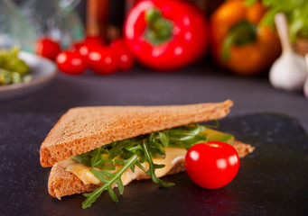 Sandwich with turkey breast, cheese, lettuce, arugula, tomatoes and onion on a black plate