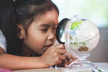 Cute asian child girl use magnifier to look and study at the globe in classroom