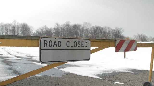 Road closed sign outside yellow blocker snow covered and trees background 