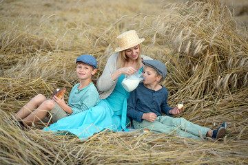 Naklejka na ściany i meble Mama feeds her sons with a roll and sips milk in a wheat field