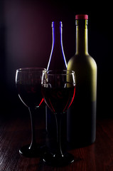 Two glasses of red wine and two bottles on dark