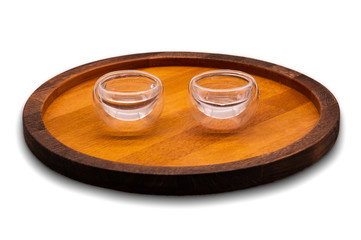 A two color wooden tray (plate) with two small glass cups with water. The colors are brown and beige (light brown). Isolated.