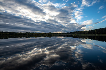 calm lake in bright sun light with reflections of clouds and trees and blue sky