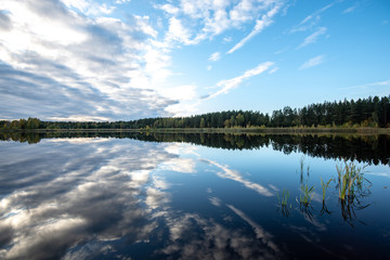 calm lake in bright sun light with reflections of clouds and trees and blue sky