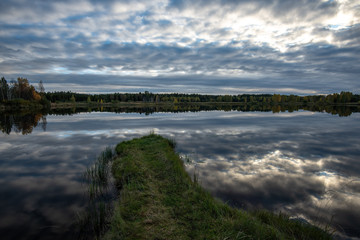 Obraz premium calm lake in bright sun light with reflections of clouds and trees and blue sky