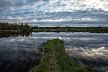 calm lake in bright sun light with reflections of clouds and trees and blue sky