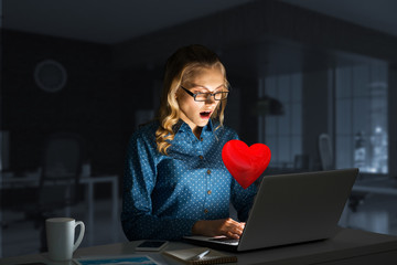 Attractive blonde wearing glasses in dark office using laptop. Mixed media