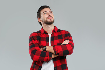 Handsome young man with a beard in a red-black checkered shirt in thought, isolated on gray background.