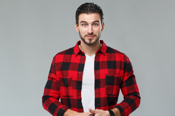 Handsome young man with a beard in a red-black checkered shirt, isolated on a gray background.