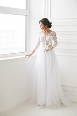 Portrait of a beautiful elegant bride waiting near a window in a bright interior.