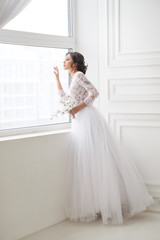 Portrait of a beautiful elegant bride waiting near a window in a bright interior.