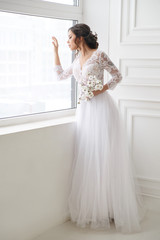 Portrait of a beautiful elegant bride waiting near a window in a bright interior.