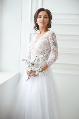 Portrait of a beautiful elegant bride with a bouquet of sakura in a bright interior.