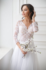 Portrait of a beautiful elegant bride with a bouquet of sakura in a bright interior.