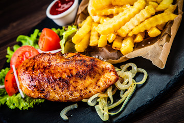 Grilled chicken fillet with french fries on wooden table