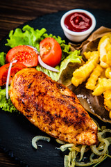 Grilled chicken fillet with french fries on wooden table