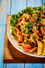 Grilled chicken meat with nachos and vegetables on wooden background