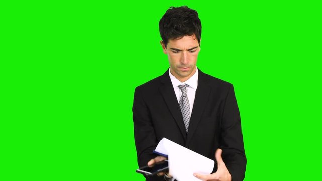 Young businessman talking on mobile phone while reading on clipboard isolated against green screen background