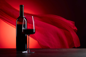 Glass and bottle of rede wine on a red background.