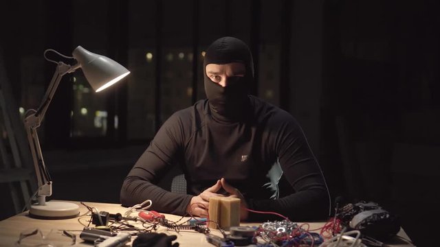 portrait terrorist wearing a balaclava mask making a bomb at night