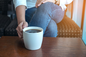Closeup image of a woman's hand holding a cup of hot coffee to drink while sitting in cafe