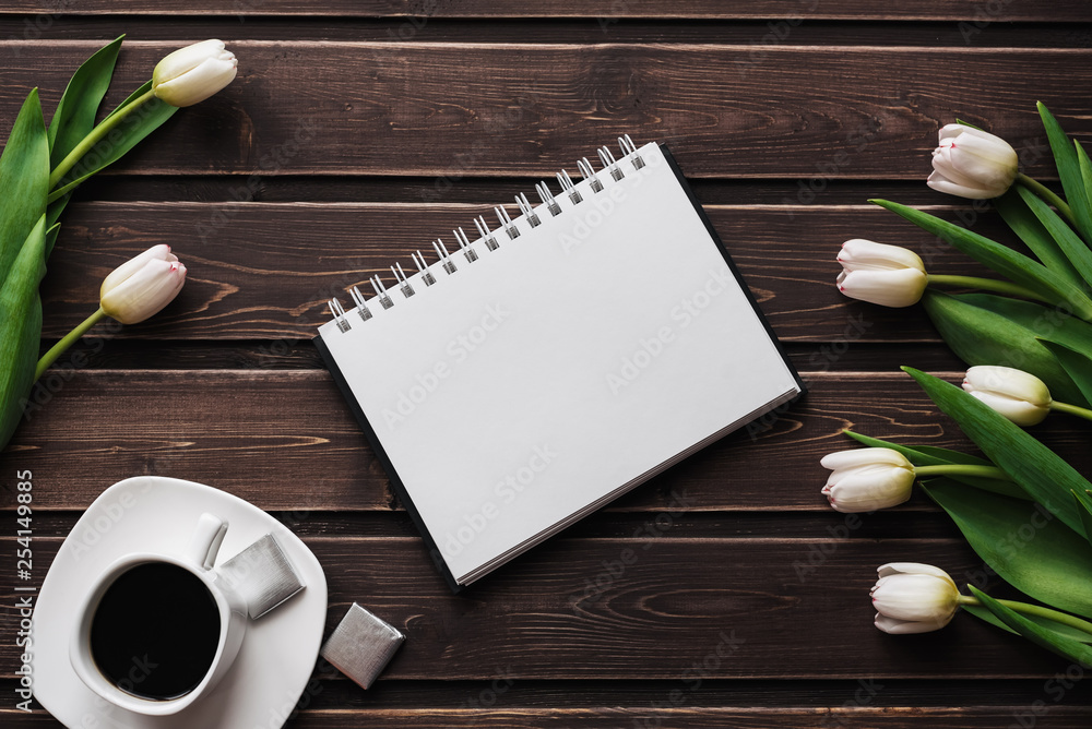Wall mural white tulips on a wooden table with a cup of coffee and an empty notebook