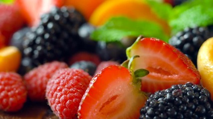 Macro closeup of rotating colorful mixed summer fruit on wooden table.