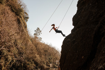 Sporty girl equipped with a rope abseiling on the sloping rock
