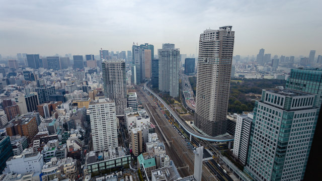 Arial view of busy Tokyo city showing dense highrise buildings, train tracks, and highways with background sky