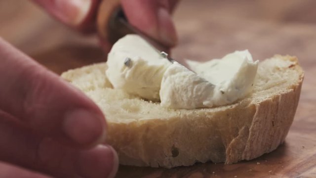 Slow motion closeup of spreading cream cheese on fresh baguette slice