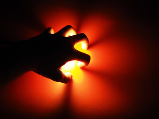 Shadow of a man's hand with yellow light on a red background. Create a flower from the light.