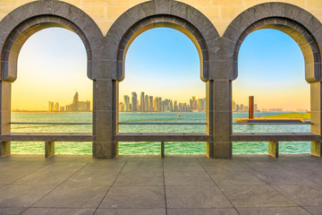 Modern skyscrapers of Doha West Bay skyline at sunset light through arches of museum located along Corniche in Qatari capital. Doha in Qatar. Middle East, Arabian Peninsula in Persian Gulf.