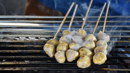 Many pork meatballs with wood stick are being grilled on an electric grill.