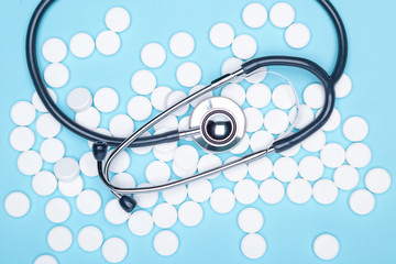 Scattered white pills on blue table.Medical, pharmacy and healthcare concept. Blue background white pills with a medical statoscope, top view.