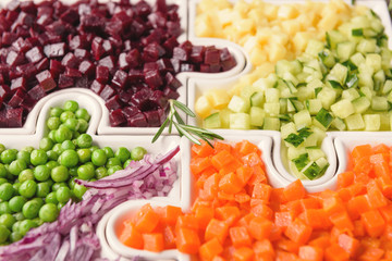 Delicious fresh pieces of vegetables of carrots, cucumber, potatoes, beets and peas close-up with fresh onion and olive oil on a bag cloth on a rustic gray table.
