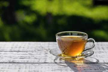 Green tea. Cup of tea with a saucer, standing on a wooden, white table, outdoors, in the rays of sunlight.