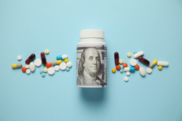 Money and pills of different colors on blue background. Rising cost of health care. - obrazy, fototapety, plakaty