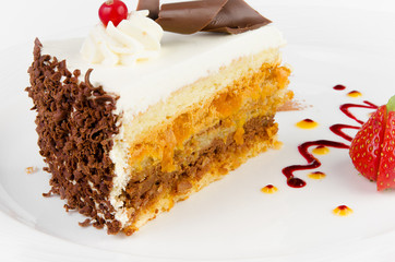 Beautiful sponge cake with dried apricots and cream in a plate with strawberries and red currants on a white background