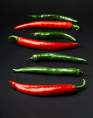 Green and red chili peppers on black background. Hot spicy food symbol.