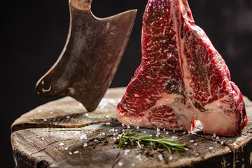 Fresh raw t-bones steak on an wooden board with sea salt and a kitchen ax.