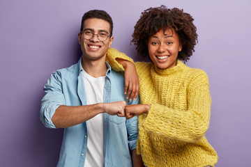 Young diverse couple give fist bump, agree to bring plan to life, smile broadly, have mixed race...