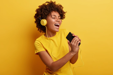 Joyful optimistic glad black woman glad to search favourite composition on web page, listens...