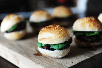 Six freshly cooked burgers on a wooden board. Sesame bun, beef cutlet, spinach greens and berry sauce.
