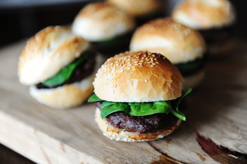 Six freshly cooked burgers on a wooden board. Sesame bun, beef cutlet, spinach greens and berry sauce.