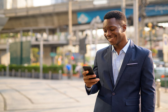 Young happy African businessman using phone in the city