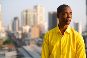 Young bald African businessman thinking against view of the city